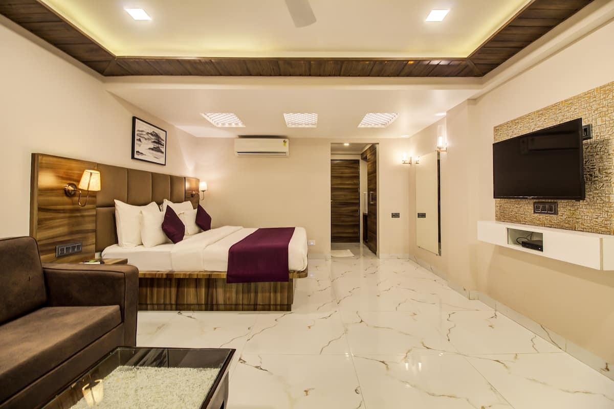 A hotel room with a bed, a sofa, a TV mounted on the wall, and a ceiling with recessed lighting.