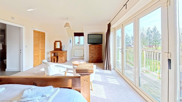 A bedroom with a large window, a TV, a wooden desk, a chair, and a bed.