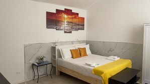 Quarto com cama, mesa de cabeceira, pequena mesa, um quadro e guarda-roupa.