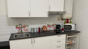 Cozinha com armários brancos, bancada preta, pia, micro-ondas e um pequeno armário com utensílios de cozinha.