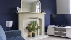 A living room with a white fireplace, a large mirror, a flat-screen TV, and a potted plant. - Raploch House (Larkhall)