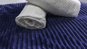 A neatly folded white towel and a rolled-up towel on a dark blue textured bedspread in a hotel room. - Raploch House (Larkhall)