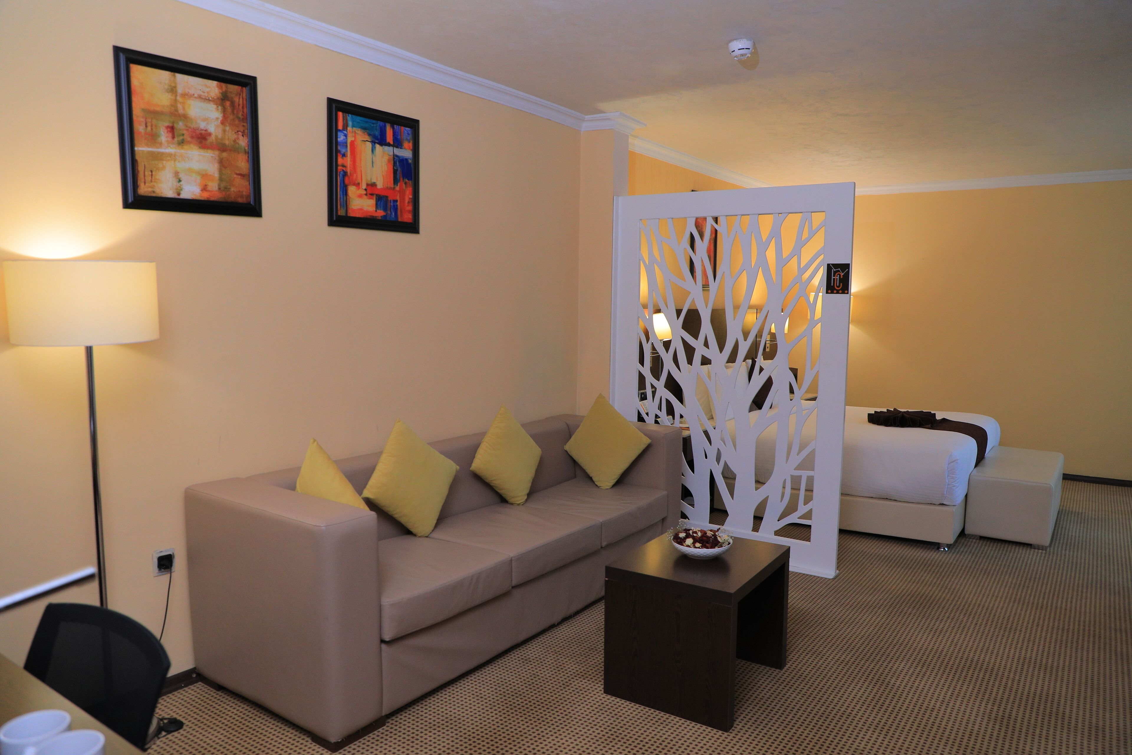 A hotel room with a beige sofa, a small table, and a decorative partition with a tree design.
