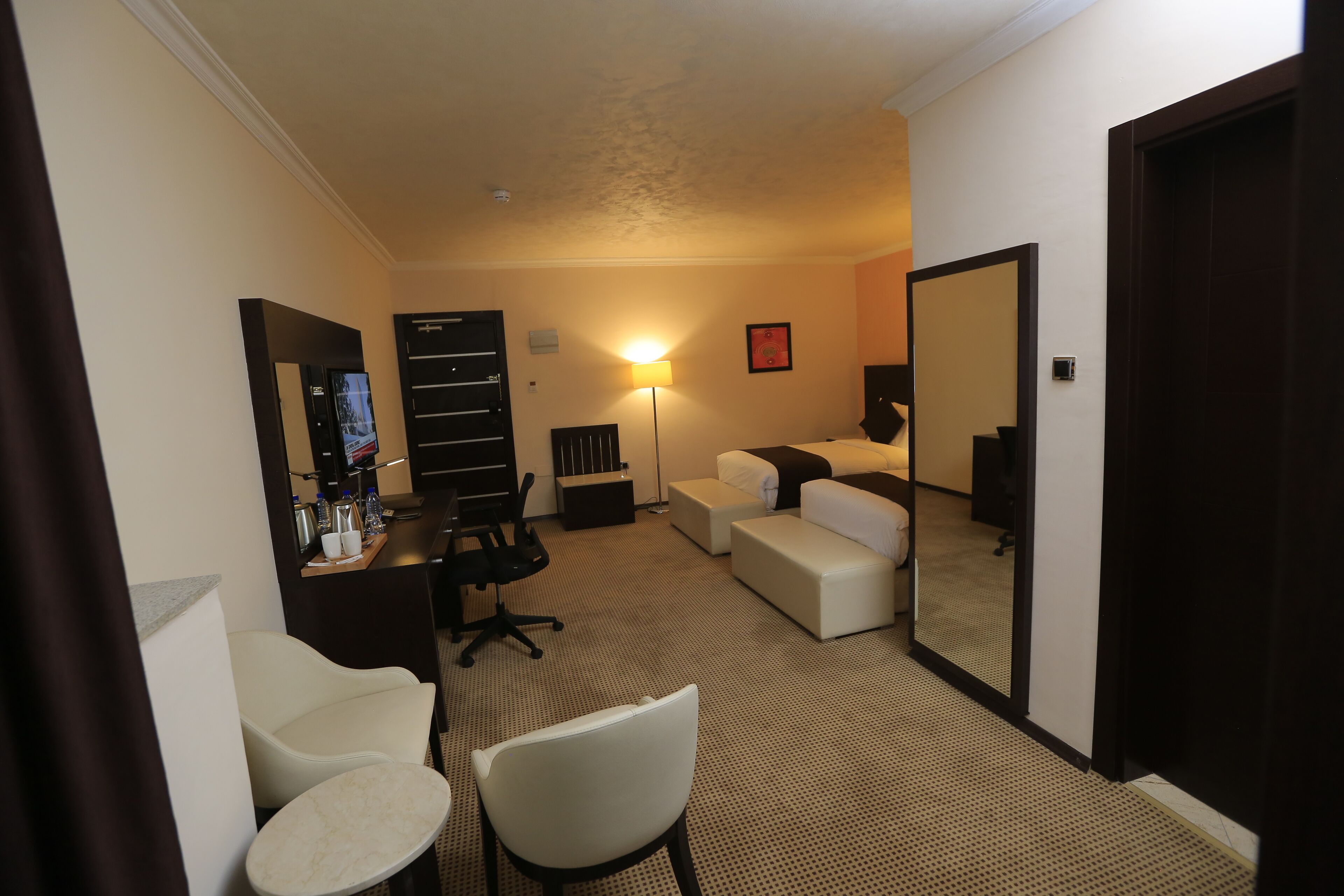 Una habitación de hotel con escritorio, silla, sofá y un espejo grande.