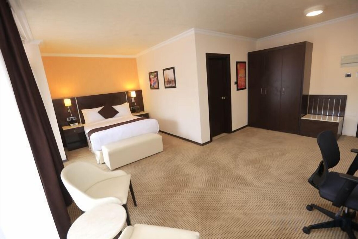 A hotel room with a bed, two chairs, a desk, and a wardrobe.