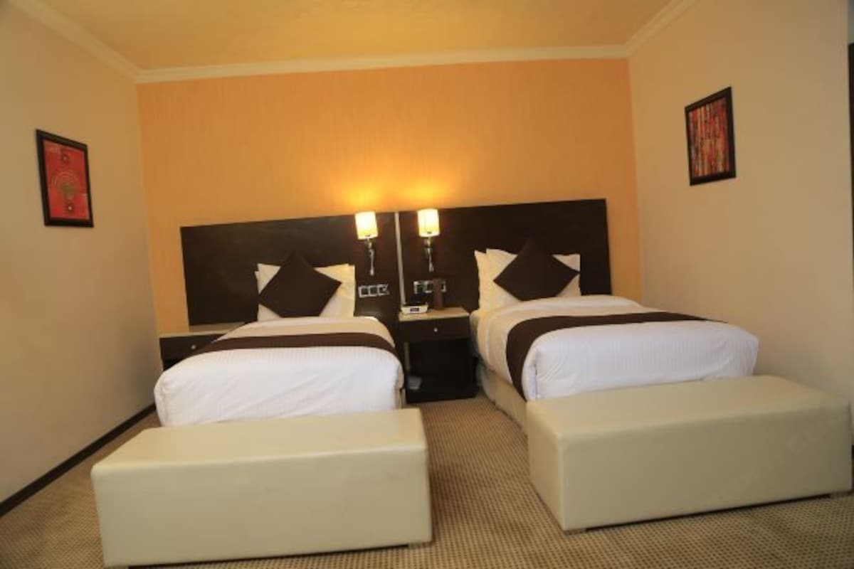 A hotel room with two beds, a nightstand, a lamp, and a framed picture on the wall.