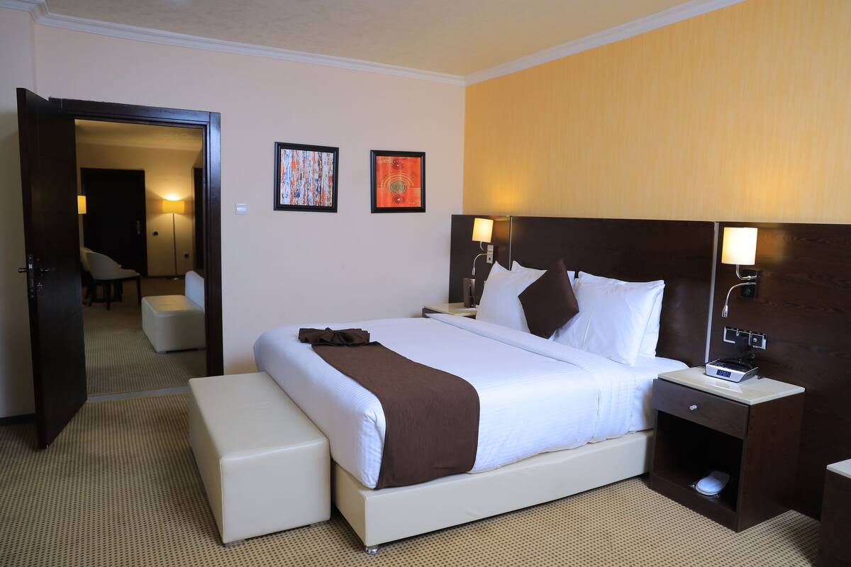 A hotel room with a large bed, bedside tables, a nightstand, a chair, and two framed pictures on the wall.
