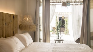 A bedroom with a large bed, a hanging light fixture, and a view of an outdoor area with plants and a chair. - 120 Hotel Boutique (Ciutadella de Menorca)