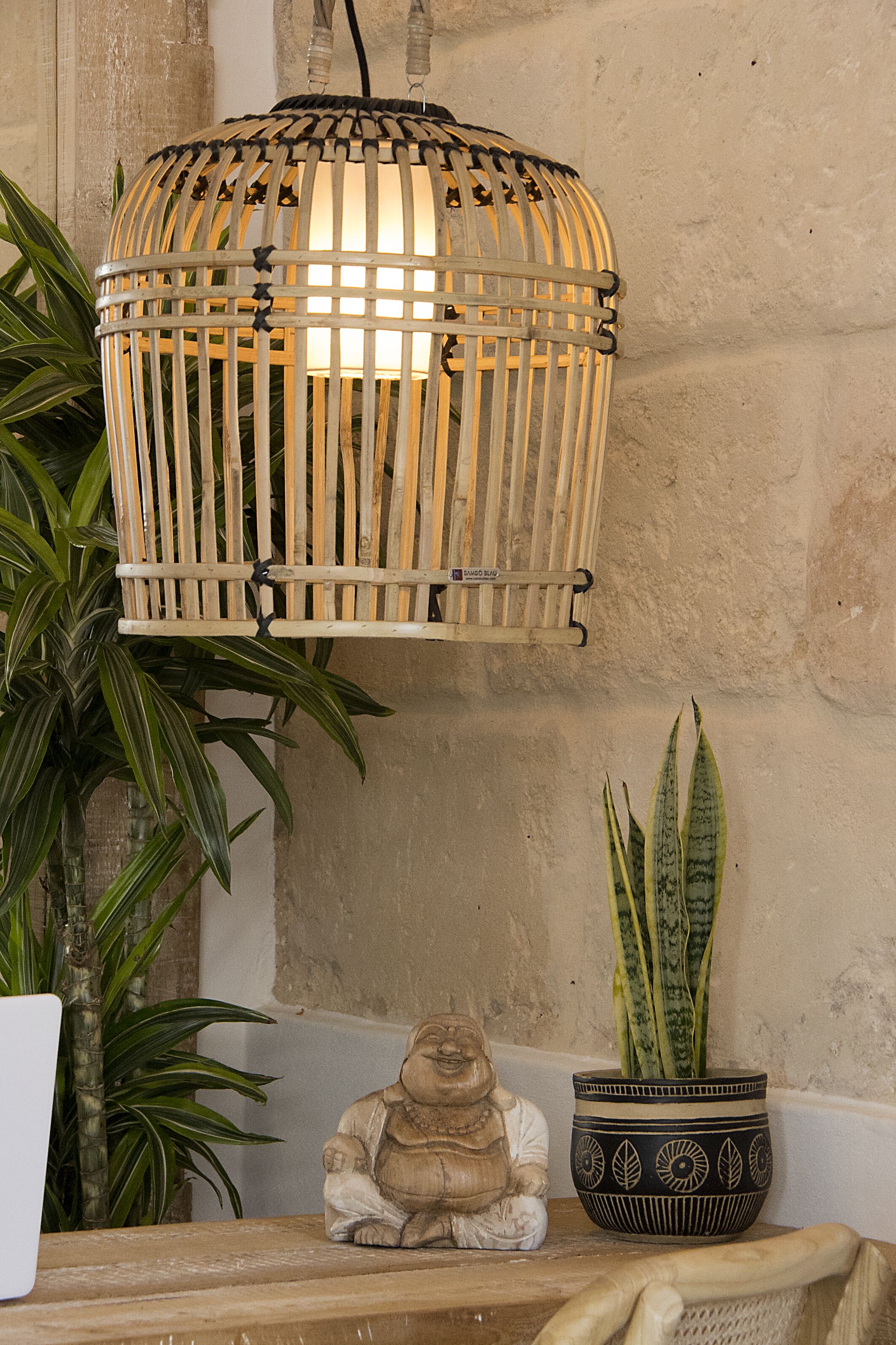 A wicker lamp hanging above a table with a Buddha statue and a potted plant.