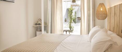 A bedroom with a bed, white bedding, a hanging light fixture, and a view of an outdoor area with a plant and a chair.