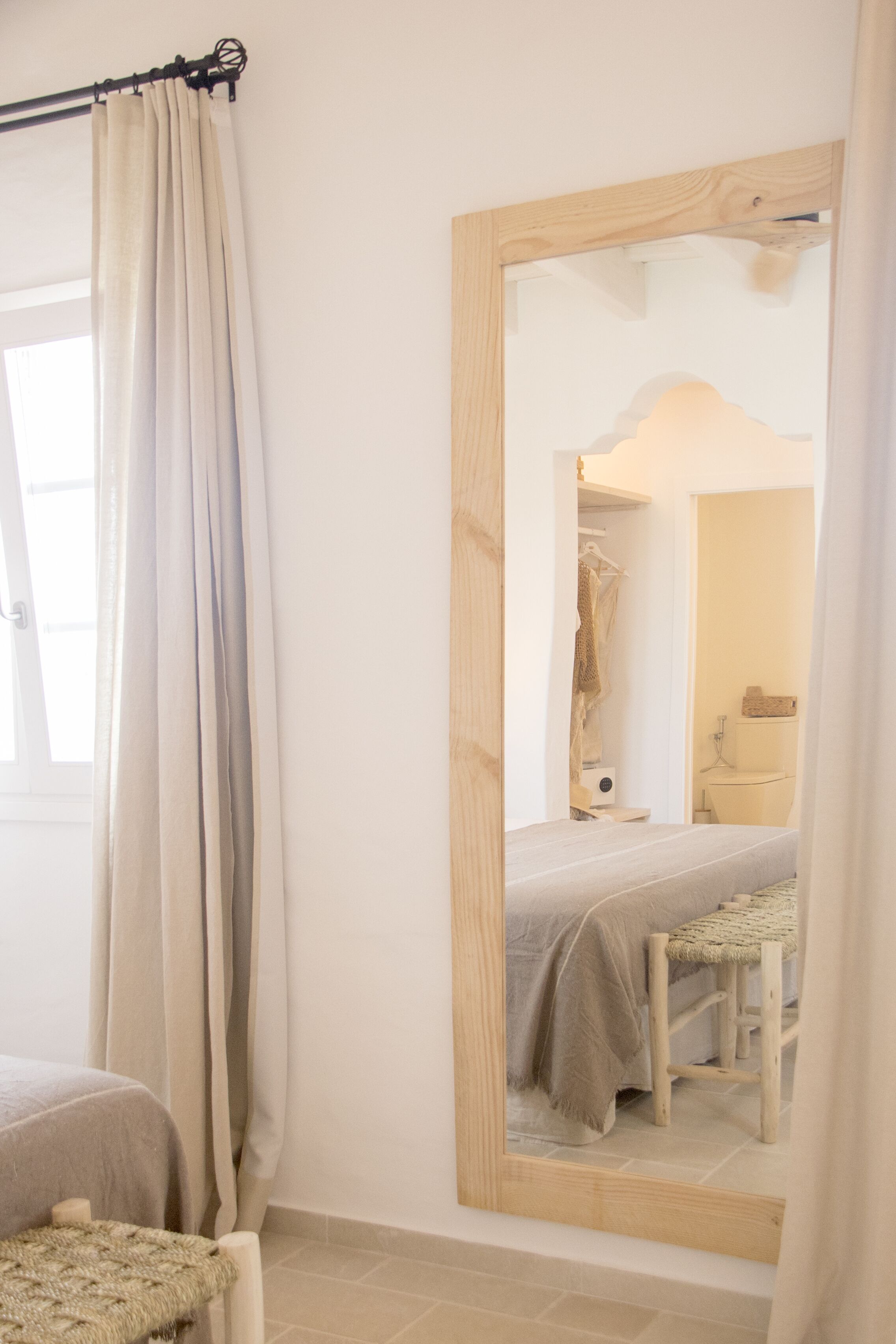 A bedroom with a bed, a chair, a mirror, and a window with curtains.