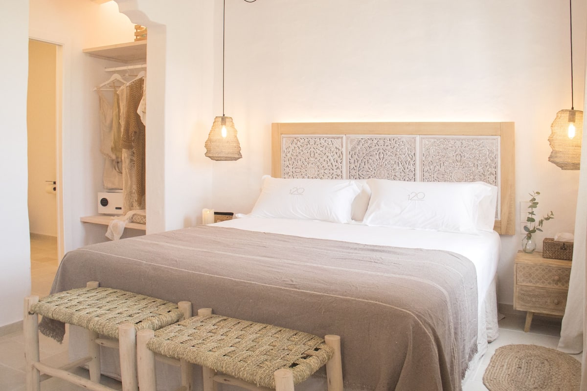 A neatly arranged bedroom with a large bed, two bedside tables, a wardrobe, and a bench.