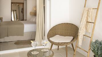 A bedroom with a bed, a wicker chair, a small table with two glasses, and a ladder against the wall.