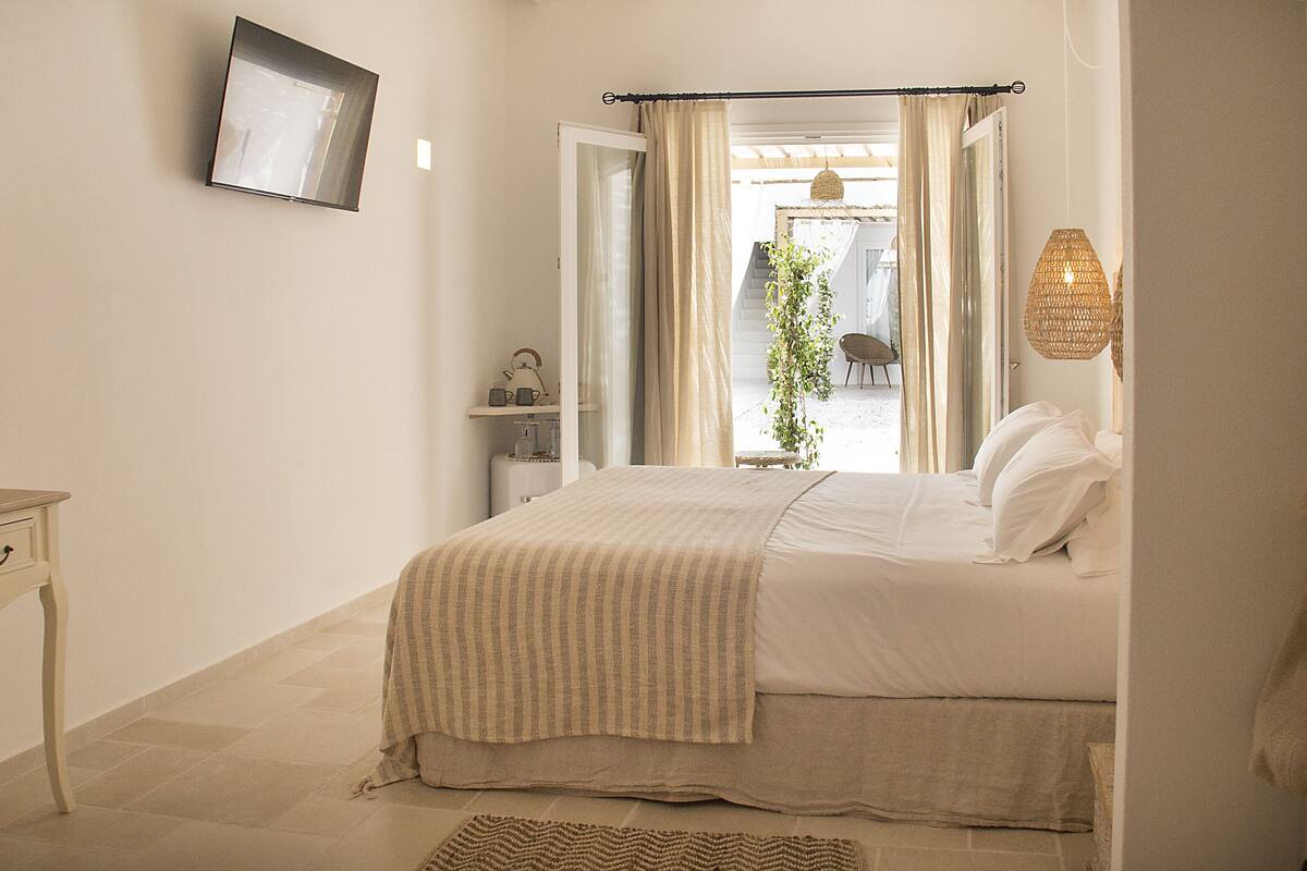 A bedroom with a bed, bedside table, chair, and a view of the outside.