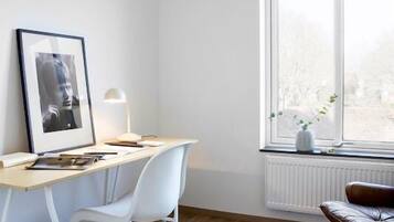 A modern, minimalist office space with a wooden desk, white chairs, a hanging pendant light, and a view of the outdoors through a large window.