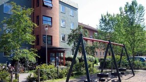 Un parque infantil con columpios y un neumático colgante, rodeado por una cerca de malla metálica.