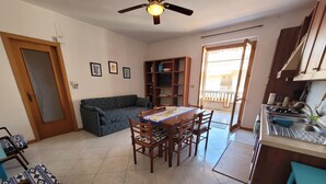 Un soggiorno con divano, un tavolo da pranzo con sedie, una ventola a soffitto e un angolo cottura con lavello e fornelli.