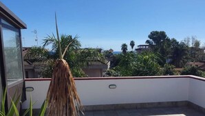 Una terrazza sul tetto con pavimento piastrellato, una pianta ricoperta di paglia e vista sul mare e sugli edifici circostanti.