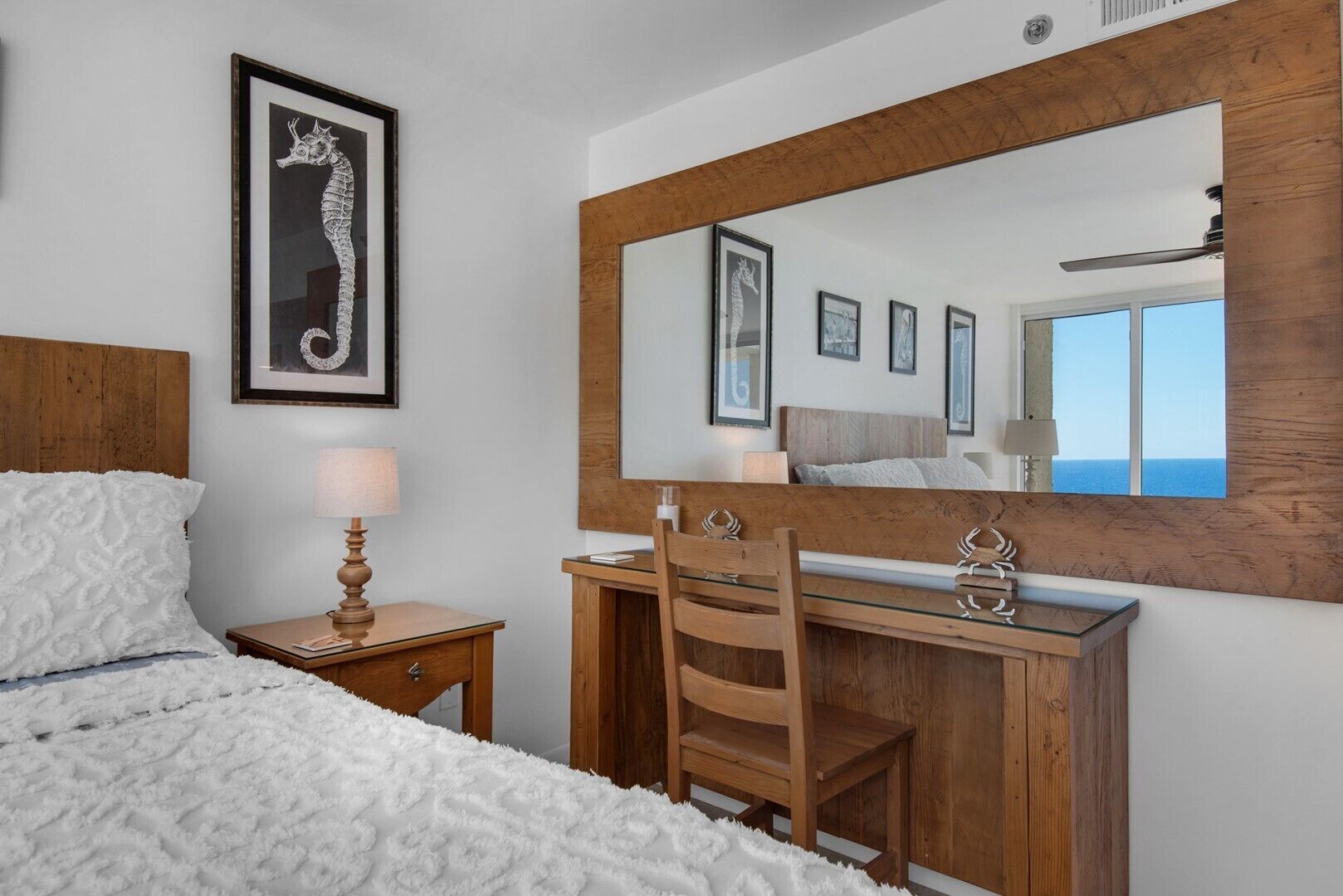 Un dormitorio con cama, una mesita de noche de madera con lámpara, un aparador de madera con espejo, y obras de arte enmarcadas en la pared.