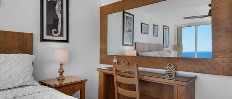 Un dormitorio con cama, una mesita de noche de madera con lámpara, un aparador de madera con espejo, y obras de arte enmarcadas en la pared.