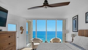 A bedroom with a large bed, two chairs, a ceiling fan, and a view of the ocean. - Stunning oceanfront condo in Panama City Beach, perfect for up to 8 guests! (Panama City Beach)