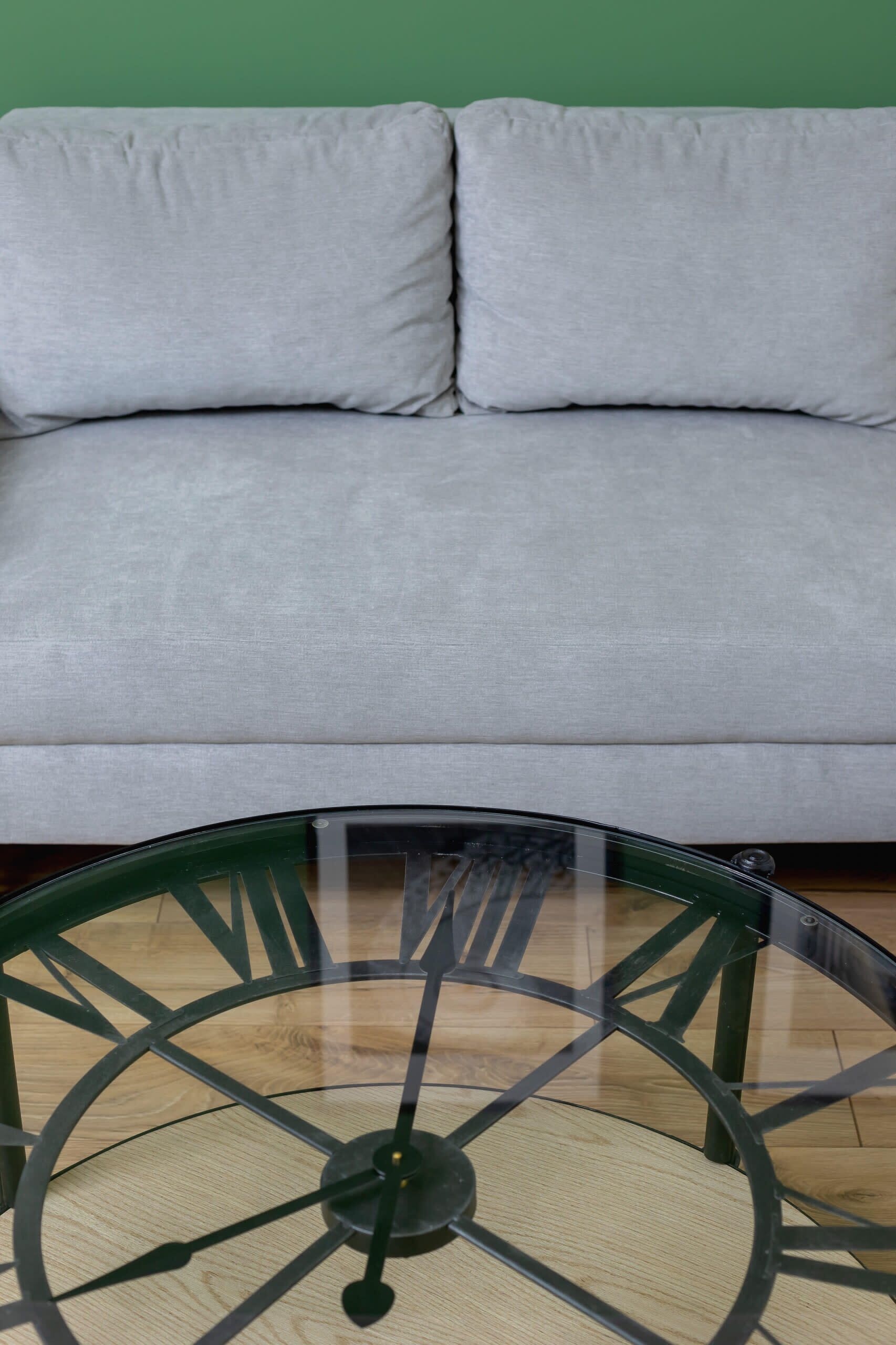 Ein runder Tisch mit einer Uhr vor einem grauen Sofa.