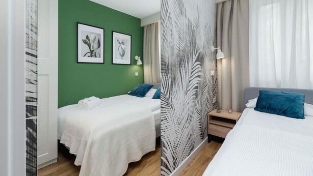A hotel room with two beds, green walls, artwork, a patterned partition, and a nightstand with a lamp.
