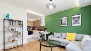 A modern living room with a glass coffee table, a grey sofa with yellow cushions, and a green accent wall.
