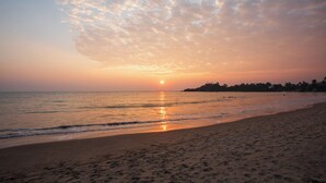 Una playa con un atardecer, mar tranquilo y huellas en la arena.
