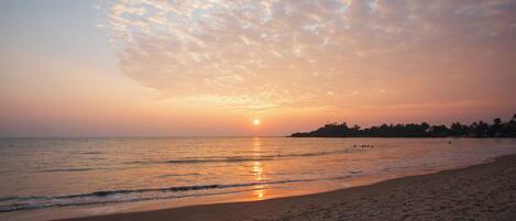 A beach with a sunset, calm sea, and footprints in the sand.