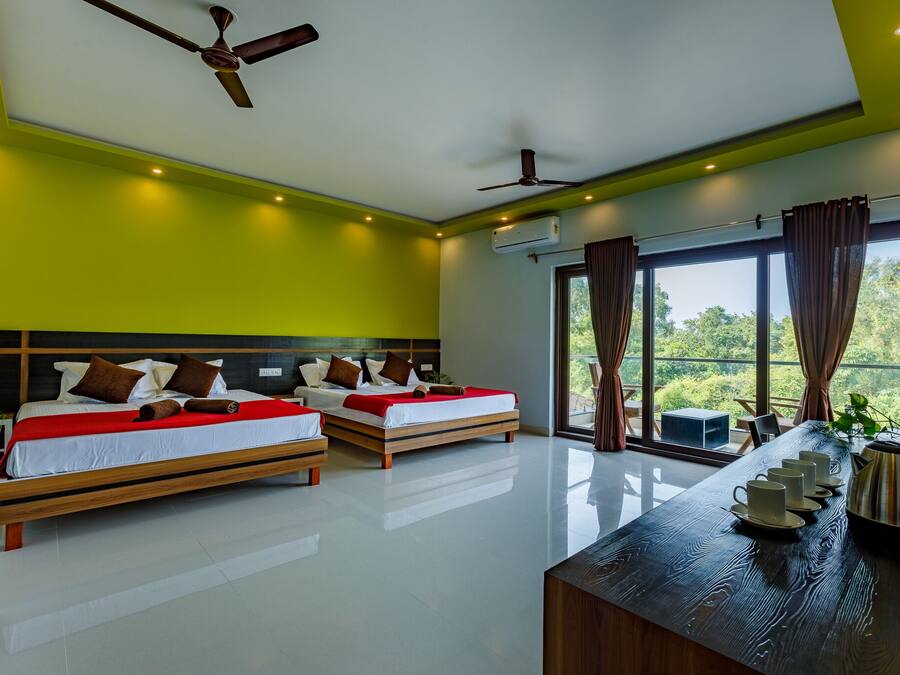 A modern hotel room with two beds, a wooden desk, and a large window offering a view of greenery.
