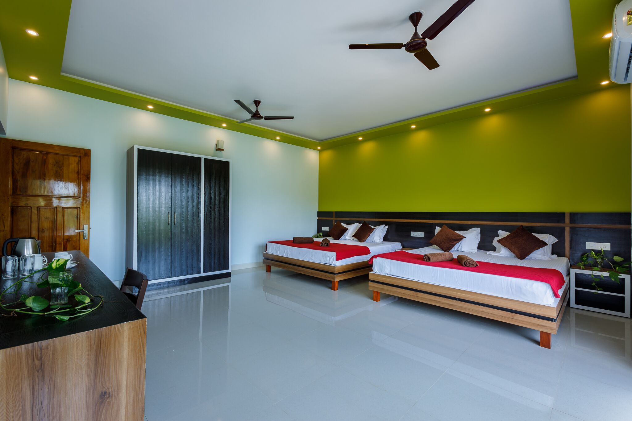 A modern bedroom with two beds, a wooden desk, and a wardrobe.