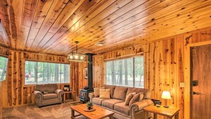 Un accogliente interno di una baita di legno con soffitto in legno, un divano, un divanetto, un tavolino da caffè e un camino.