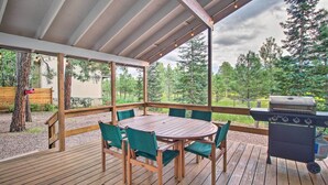 Una terrazza esterna coperta con tavolo e sedie in legno, un barbecue e vista sugli alberi.