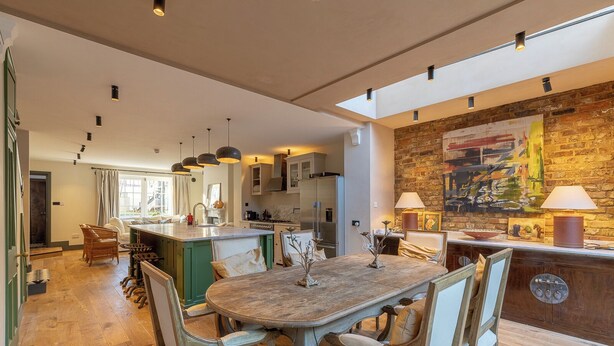 A spacious kitchen with a central island, modern pendant lighting, and a rustic brick wall with artwork.
