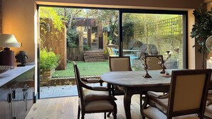 A dining area with a table and chairs, a lamp, and a view of a garden through large windows.