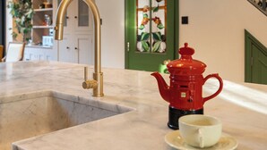 A kitchen with a marble countertop, a gold faucet, a red teapot, and a cup on a saucer.