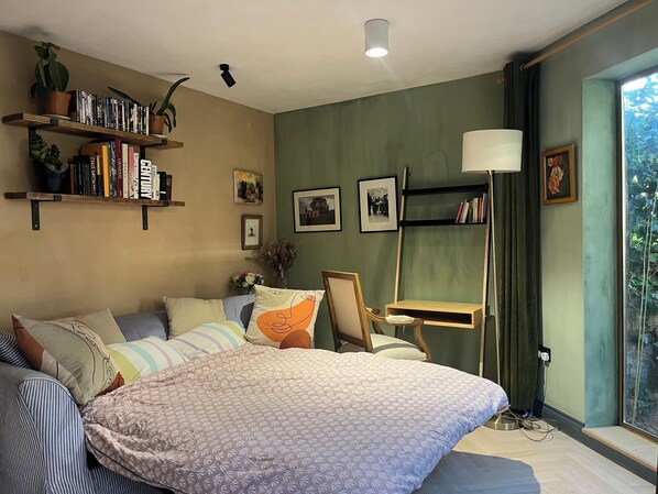 Un dormitorio con cama, escritorio, estanterías llenas de libros y ventana con vistas.