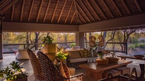 A covered outdoor seating area with wicker furniture, a wooden table, and potted plants. - Simbavati River Sands (Bushbuckridge)