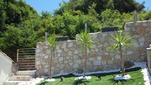 A stone wall with palm trees, a grassy area, and a metal gate. - Lovely Studio in Strinilas With its own Pool (Corfu)