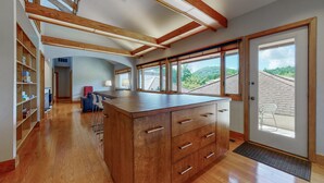 A spacious kitchen with wooden cabinetry, a central island, and large windows offering a view of the surrounding landscape.