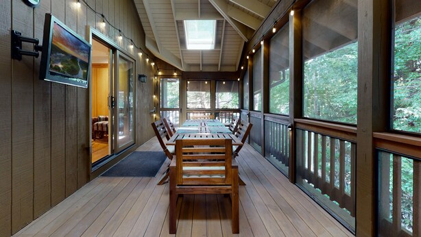 A wooden deck with a dining table and chairs, large windows, and a skylight.