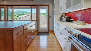 A modern kitchen with wooden cabinetry, a large island, and a view of a green landscape through the windows.