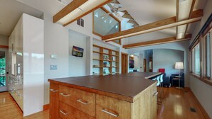 A spacious kitchen with a large island, wooden beams, a ceiling fan, and a view of the outdoors.