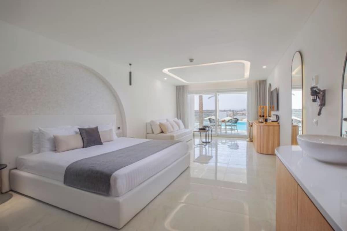 A modern hotel room with a large bed, a bathroom with a large mirror, and a view of the city through the window.