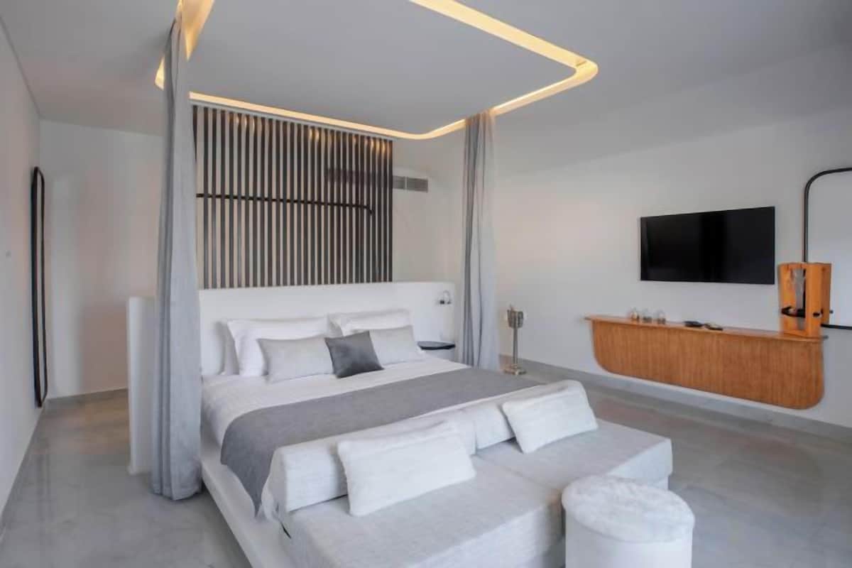 A modern bedroom with a large bed, a bedside table, a TV, and a wooden console.