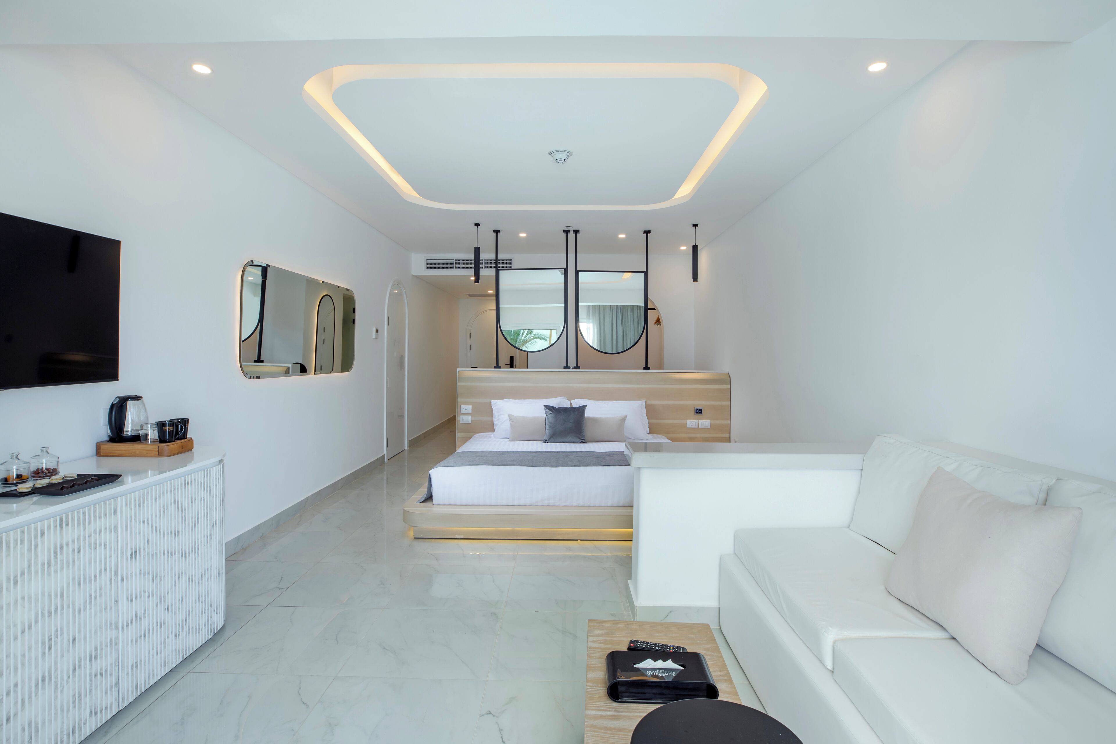 A modern hotel room with a bed, a sofa, a TV, and a coffee table.