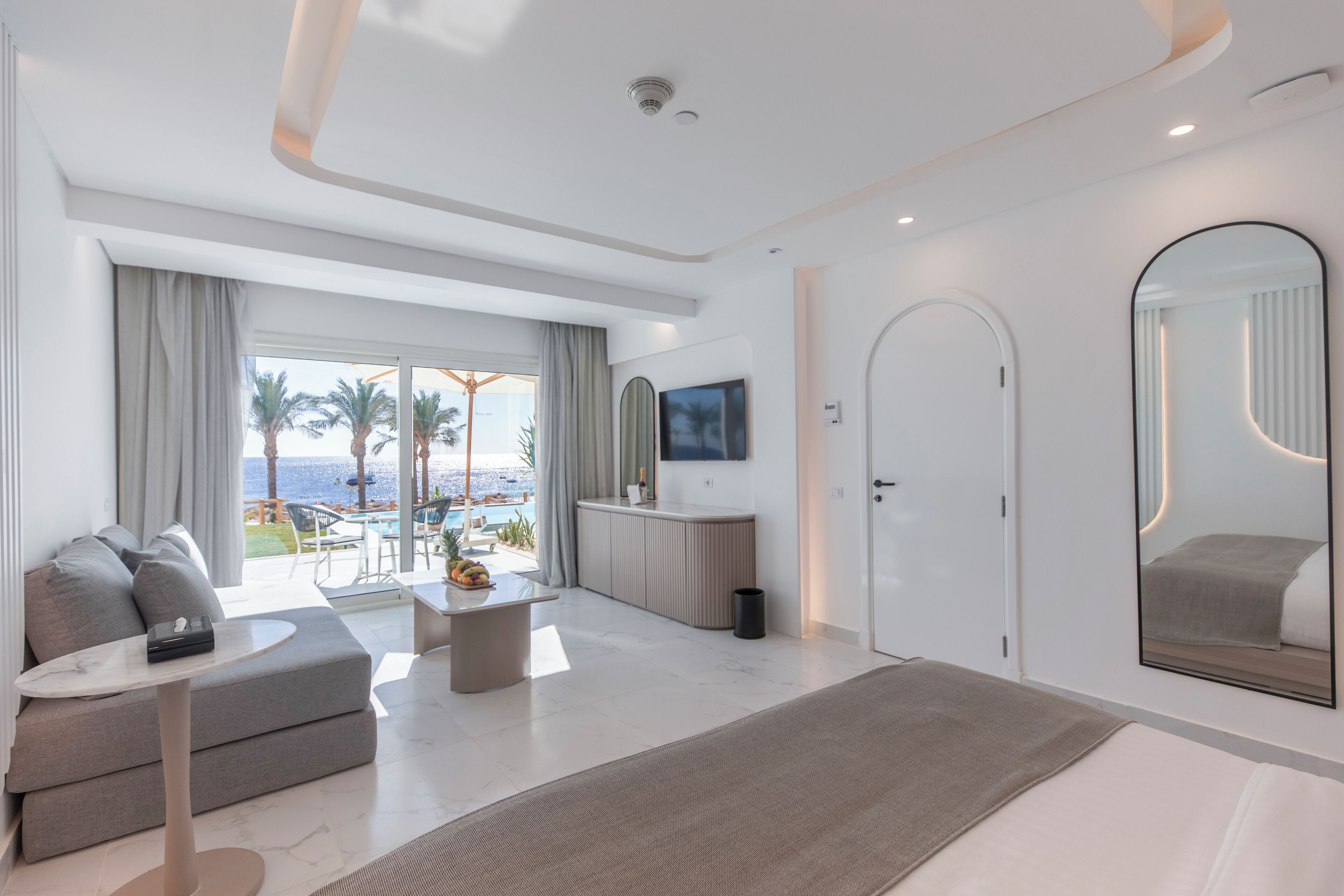 Een moderne hotelkamer met een groot bed, een slaapbank, een televisie en uitzicht op de oceaan.