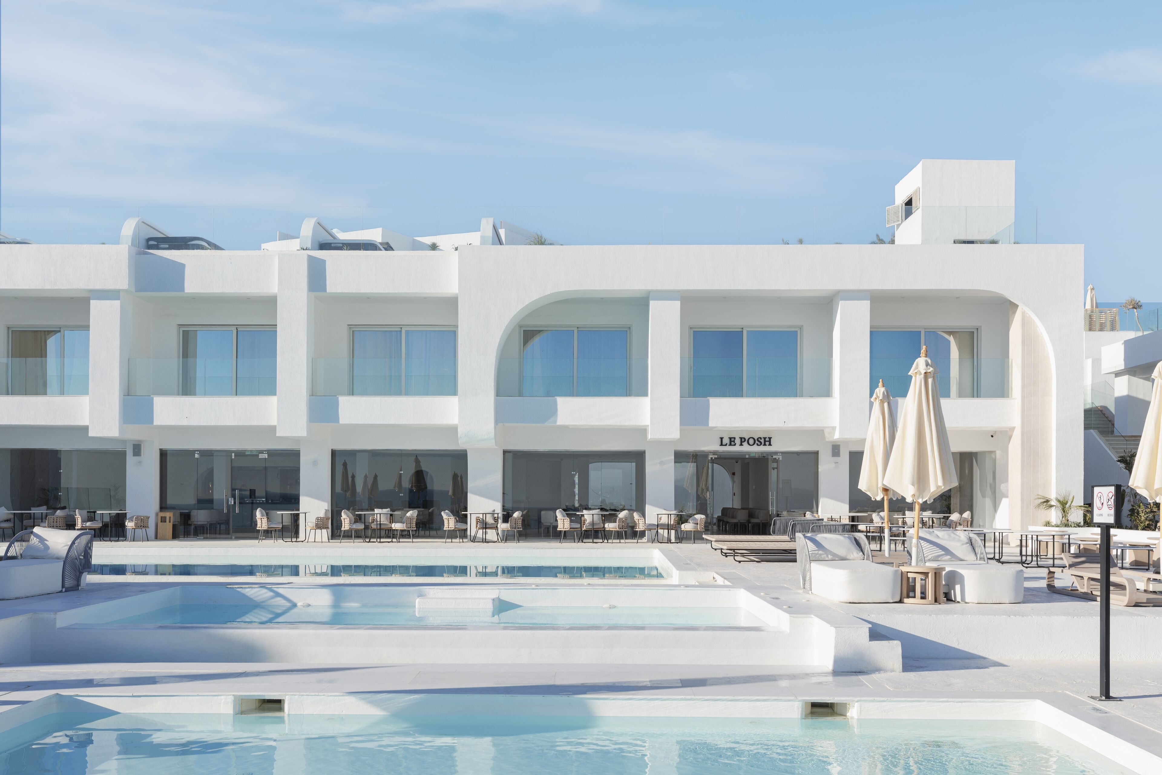 Ein modernes Hotel mit Poolbereich, Außenbereich zum Sitzen und blauem Himmel.