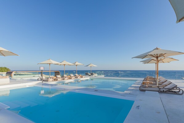 Zona junto a la piscina con sillones de descanso y sombrillas, con vistas al mar.